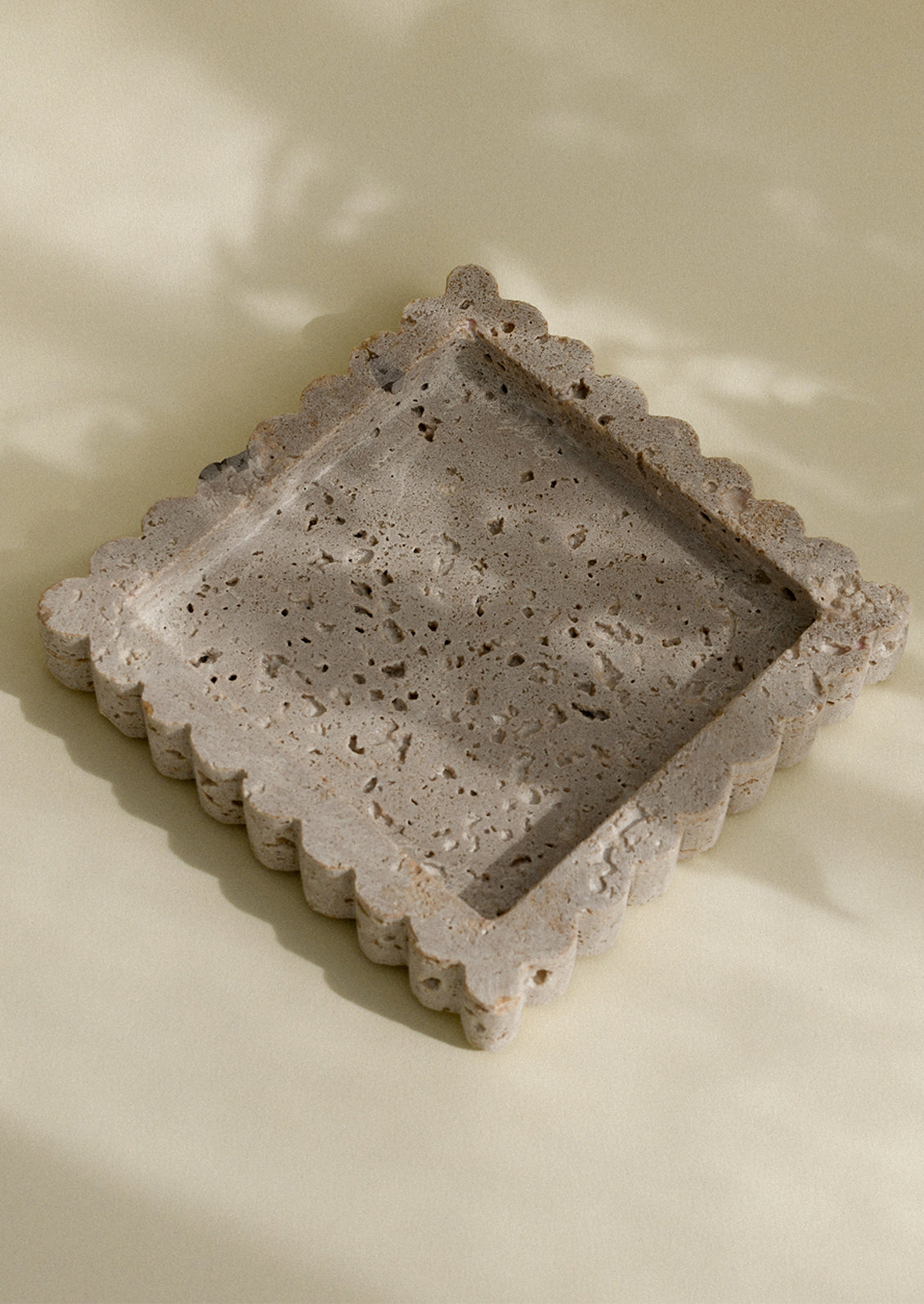 A square shaped travertine tray with scalloped edges.