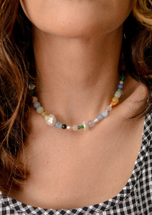 A woman wearing a necklace with colorful natural gemstones and baroque pearls.