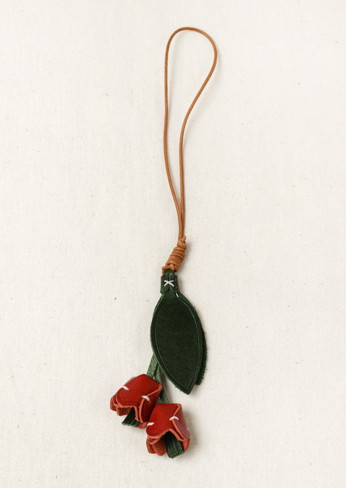 A leather bag charm shaped like a tulip with red petals and green leaves.