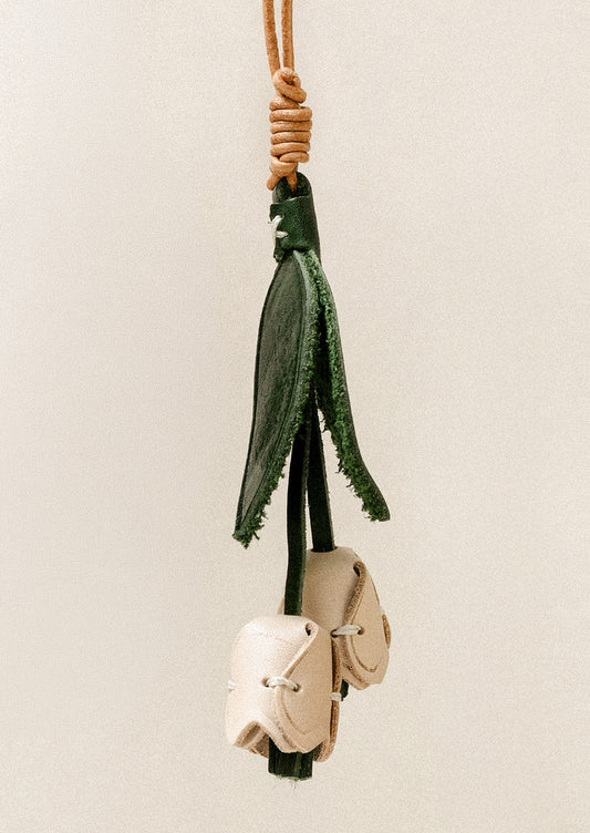 A leather bag charm shaped like a tulip with cream petals and green leaves.