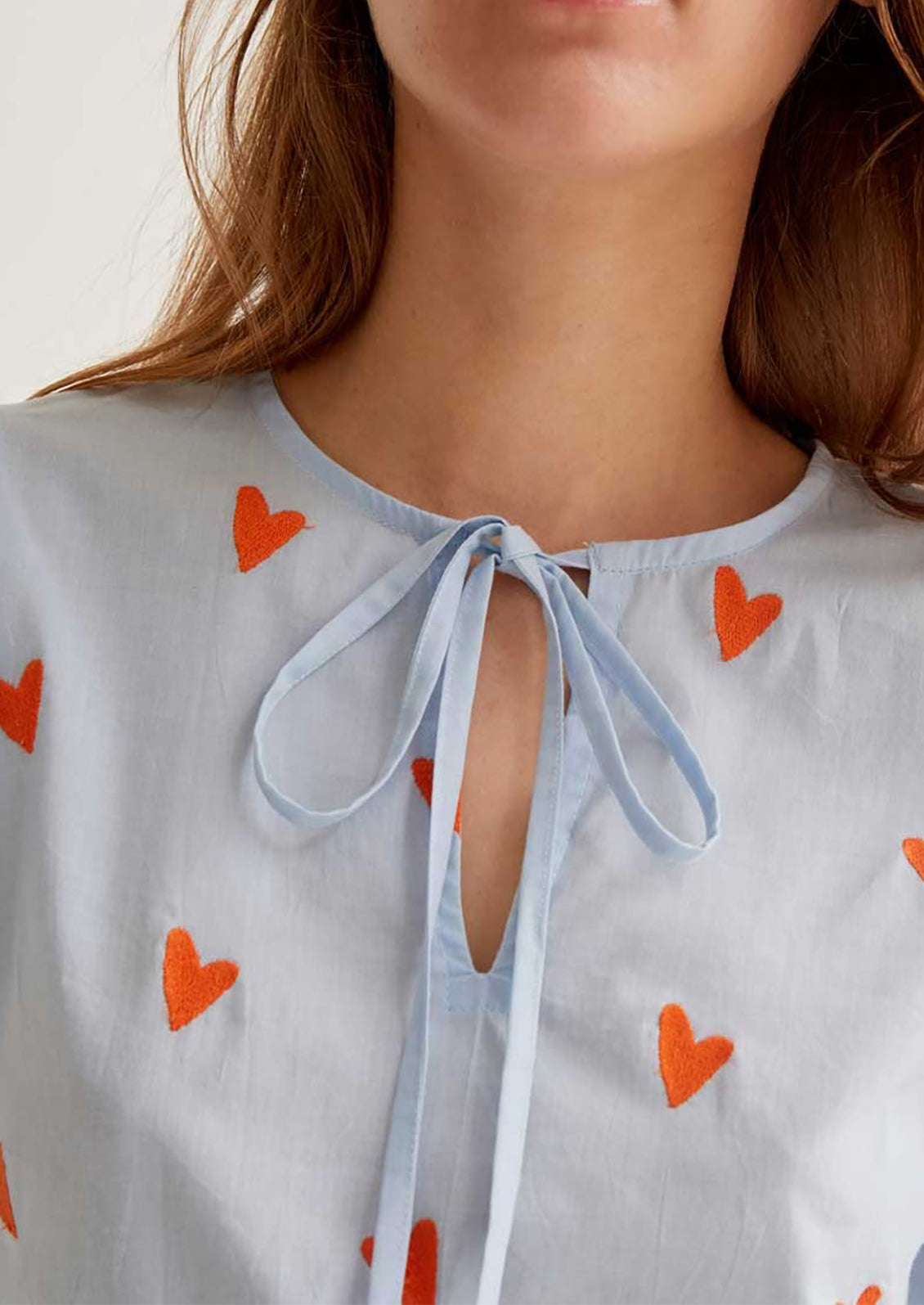Light blue blouse with orange heart patterns and a tie neckline.