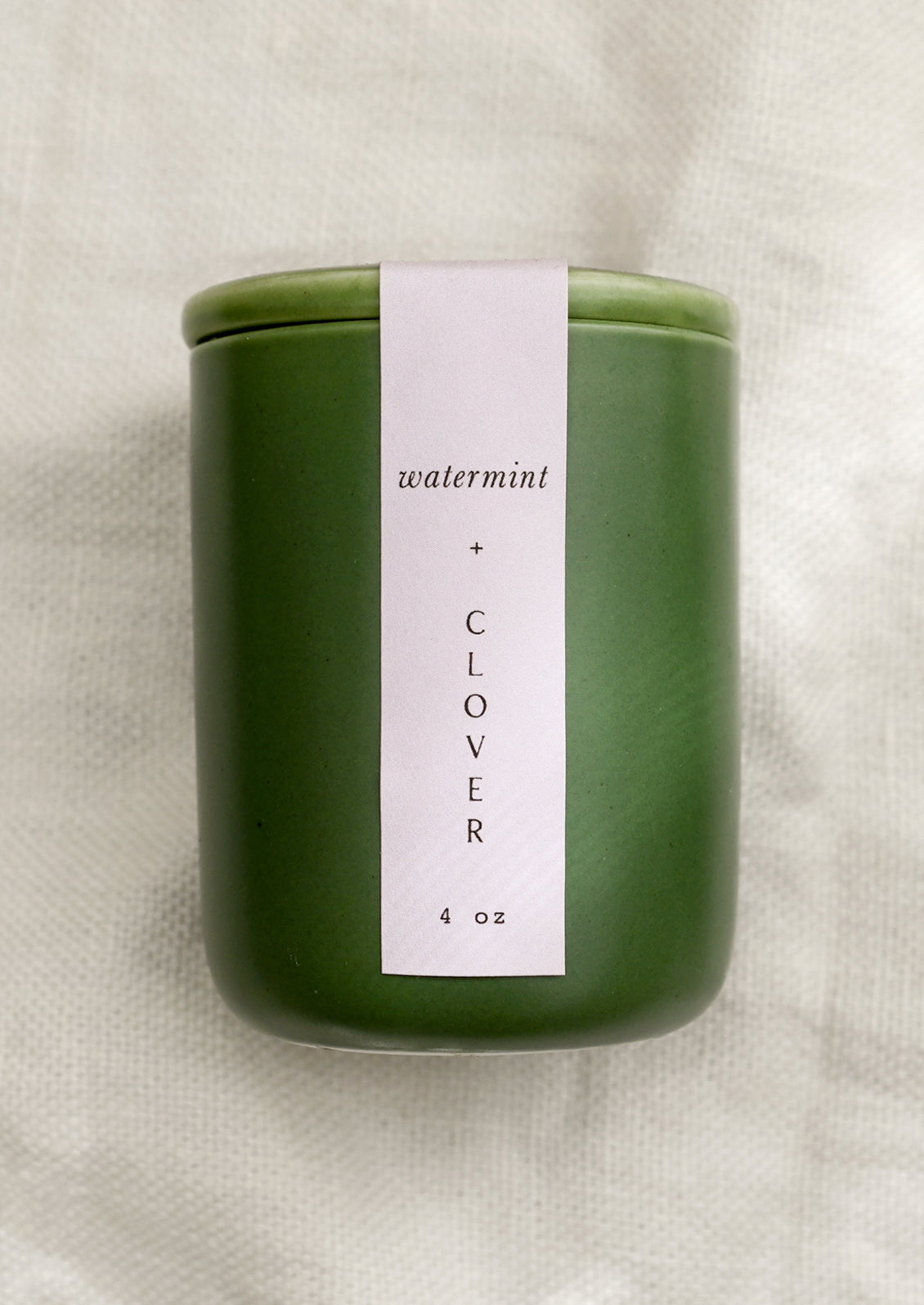 A small candle in lidded green ceramic jar in Watermint and Clover scent.
