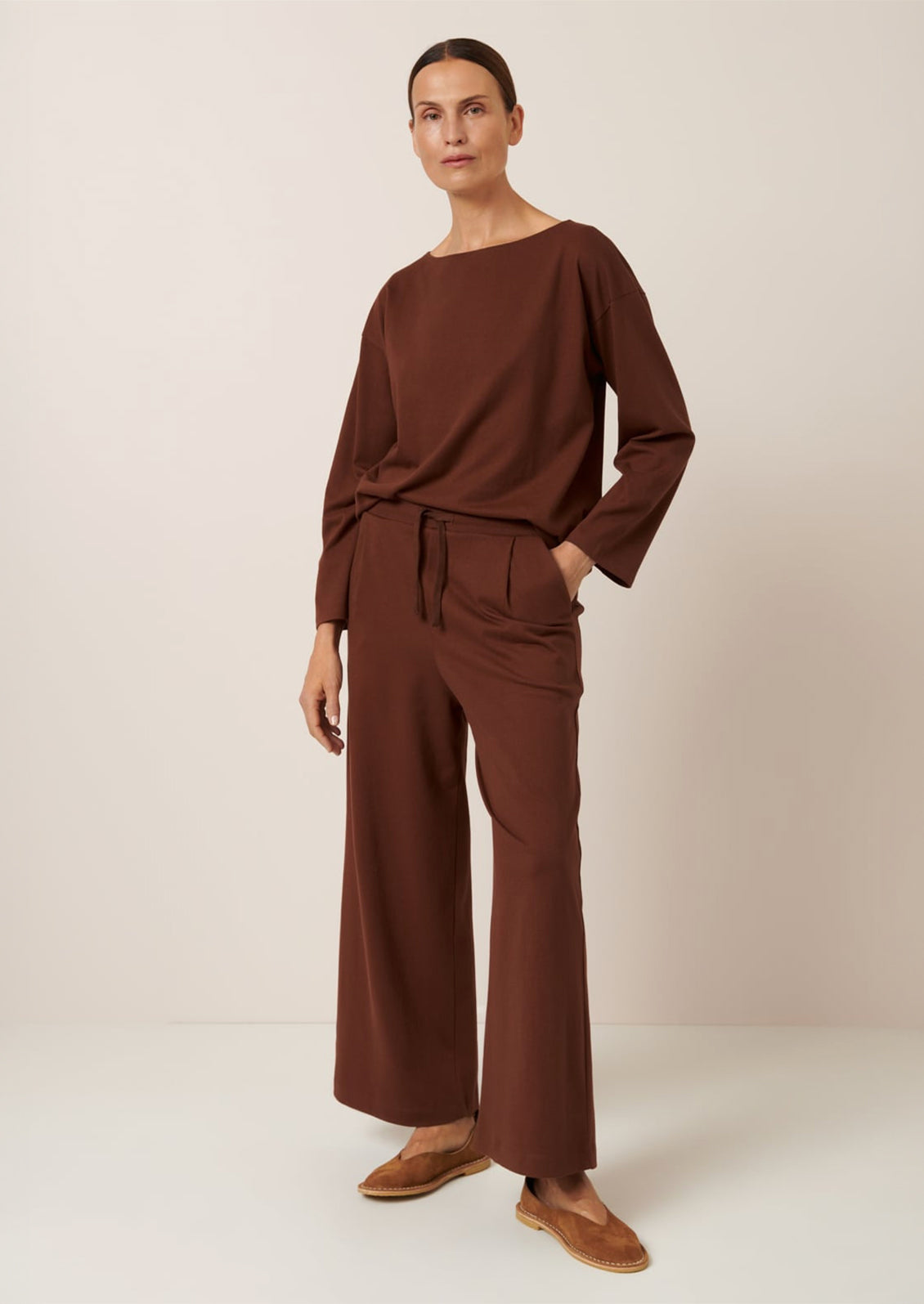 A person wearing a pair of wide leg pants in sequoia brown color.