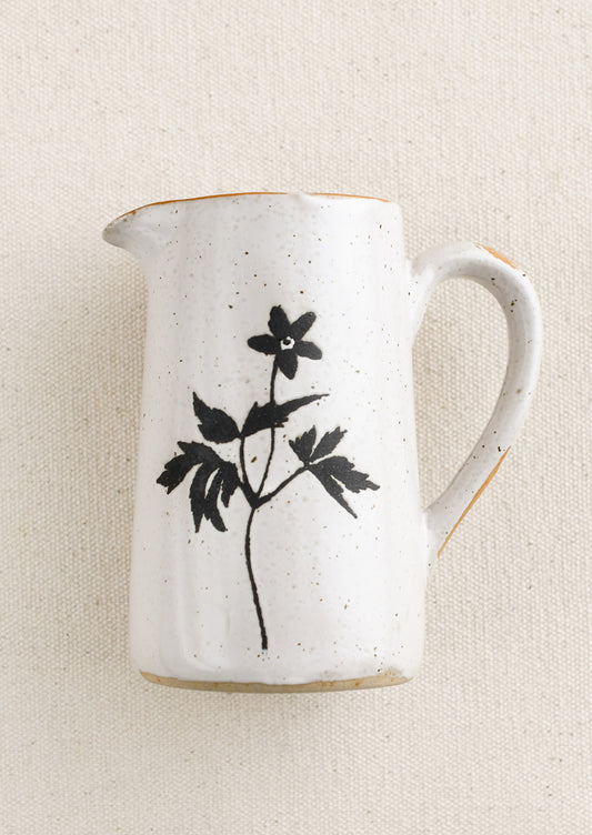 A small speckled white ceramic creamer pitcher with black flower silhouette.