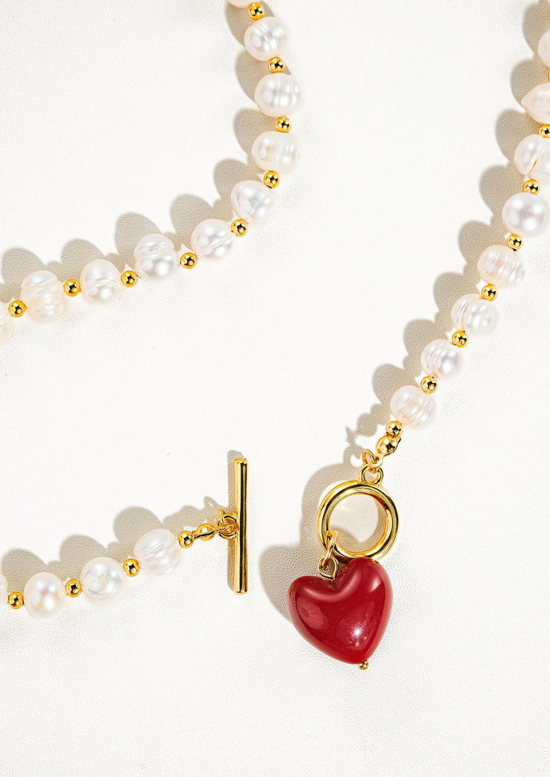 A necklace with alternating gold and pearl beads and red heart toggle clasp.