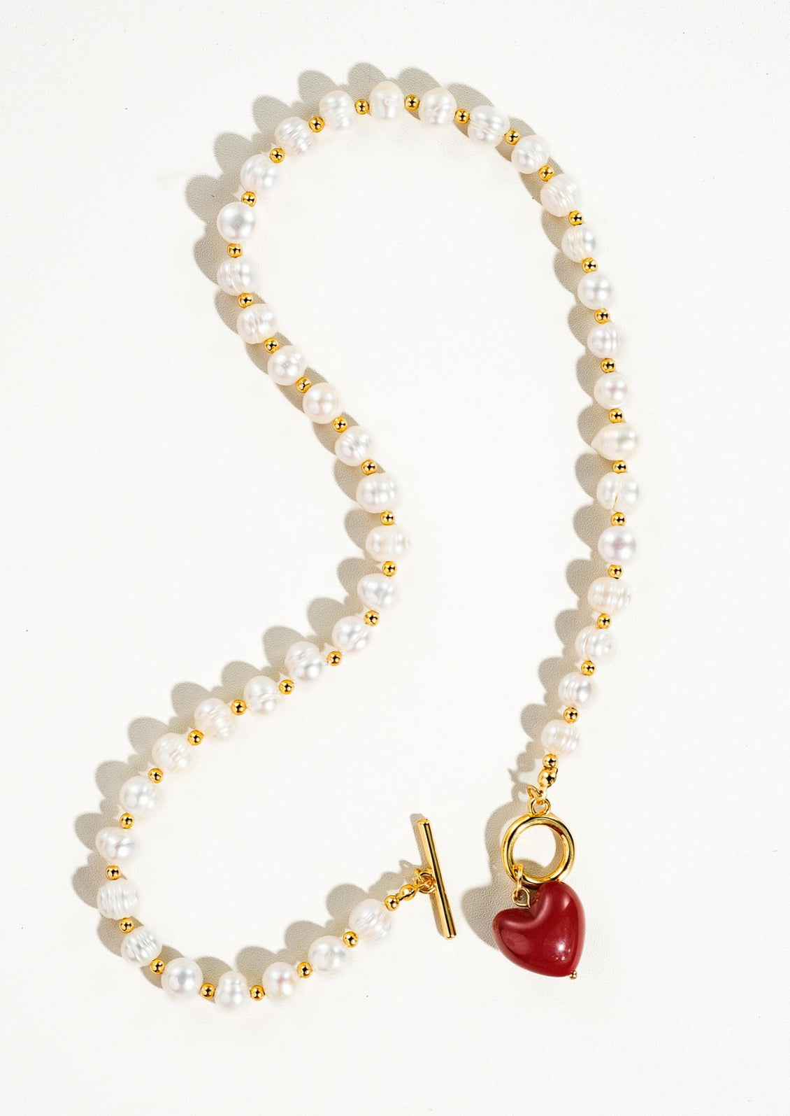 A necklace with alternating gold and pearl beads and red heart toggle clasp.