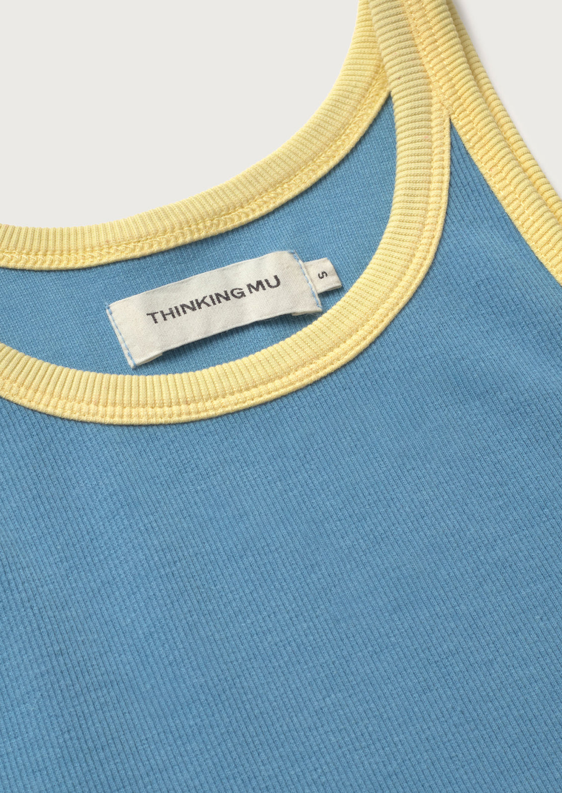 Close-up of a blue garment with yellow trim and a visible 'Thinking Mu' label.