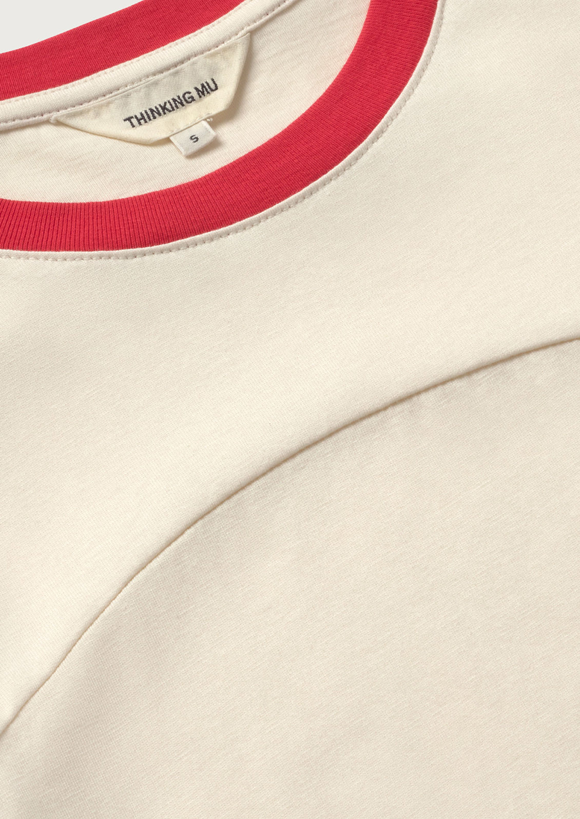 Close-up of a beige garment with red trim and 'Thinking Mu' label.