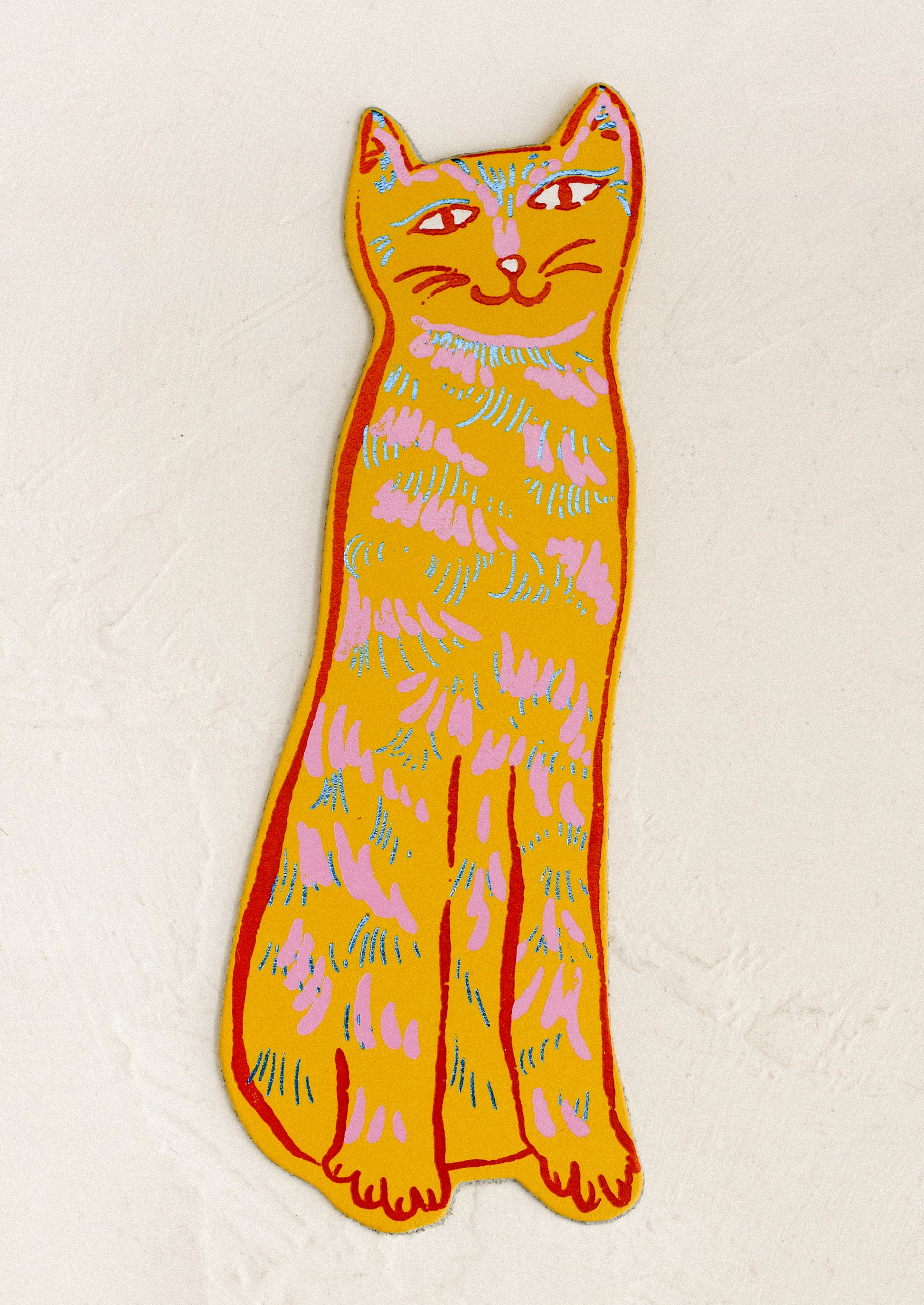A die-cut leather bookmark in the shape of a cat, in yellow color.