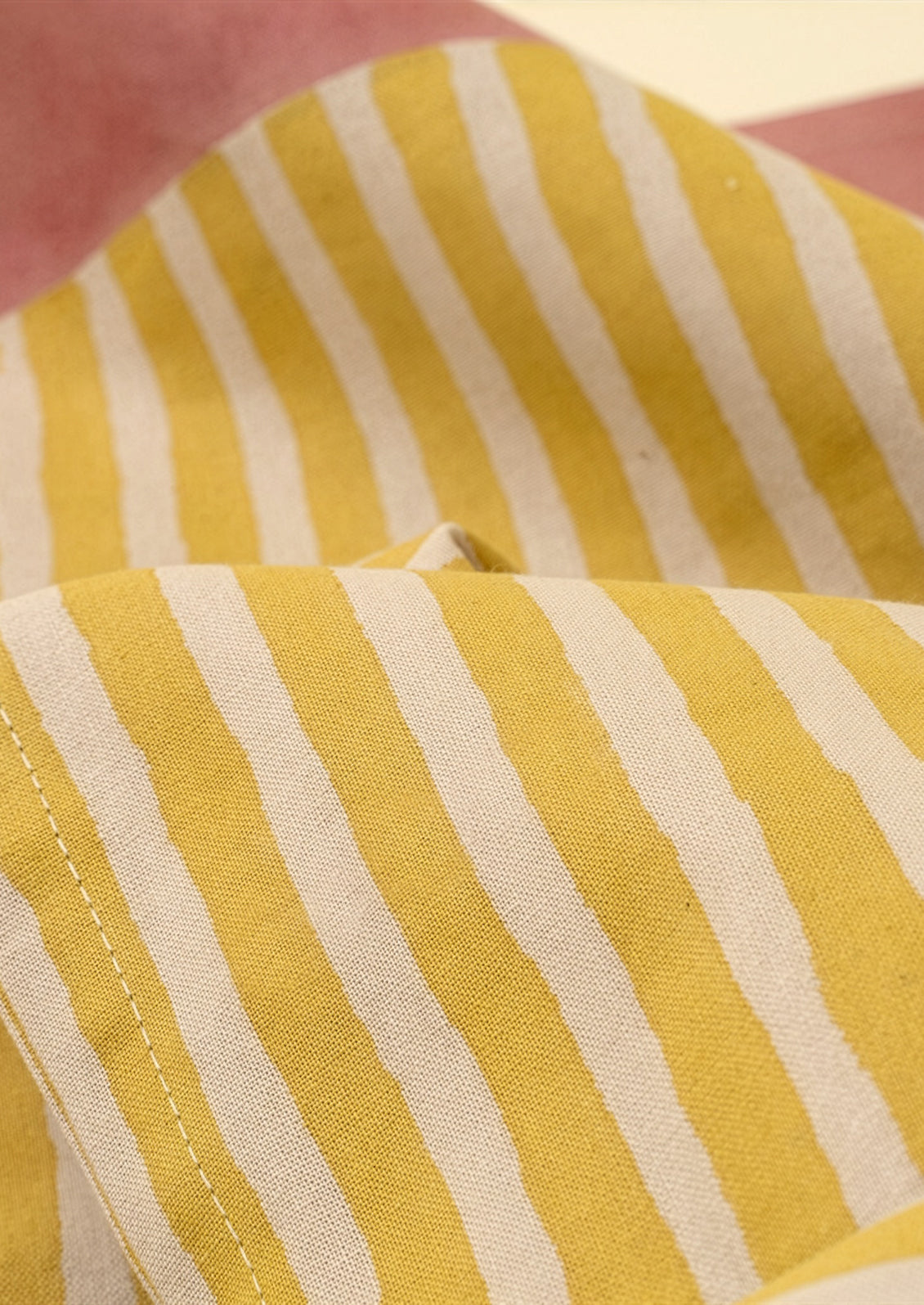 Close-up of yellow and white striped fabric with a pink background