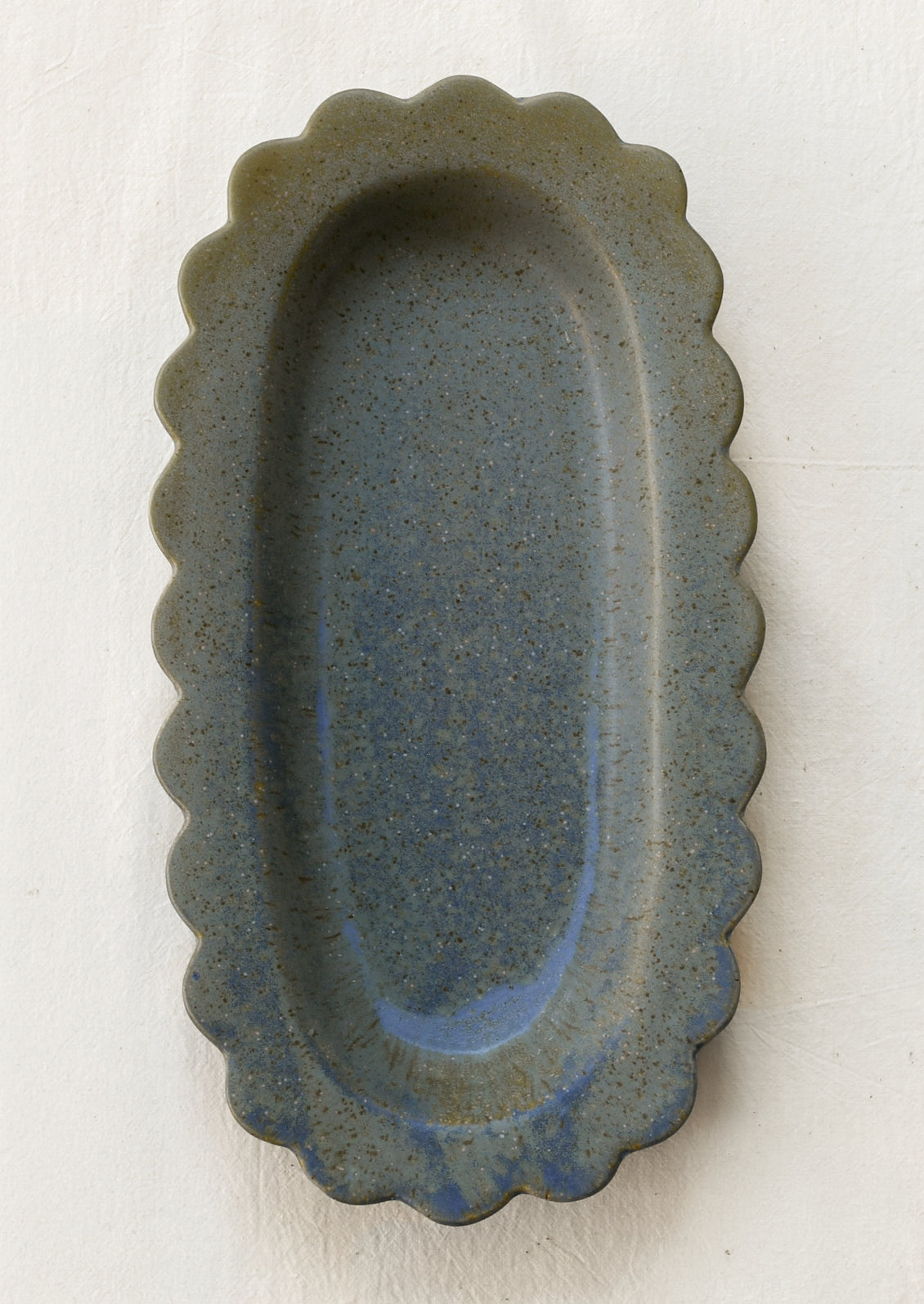 An oval-shaped scalloped stoneware tray in speckled blue.