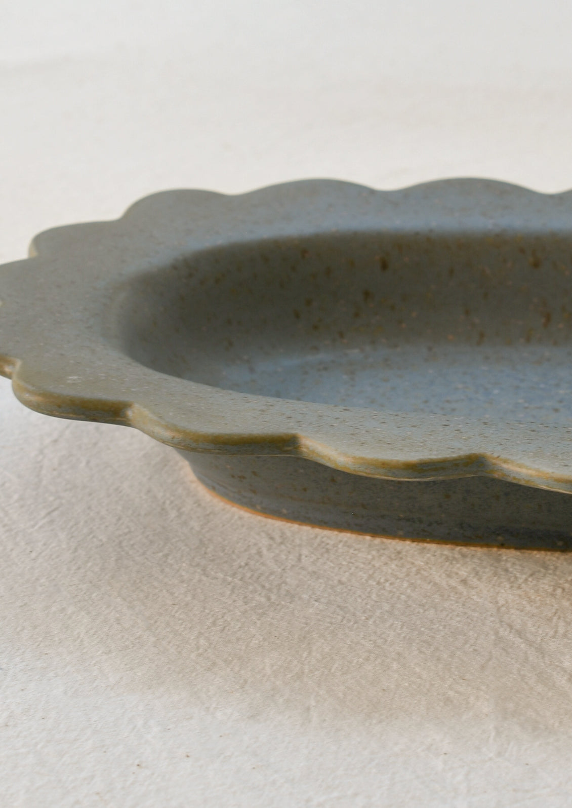 Closeup of an oval-shaped scalloped stoneware tray in speckled blue.