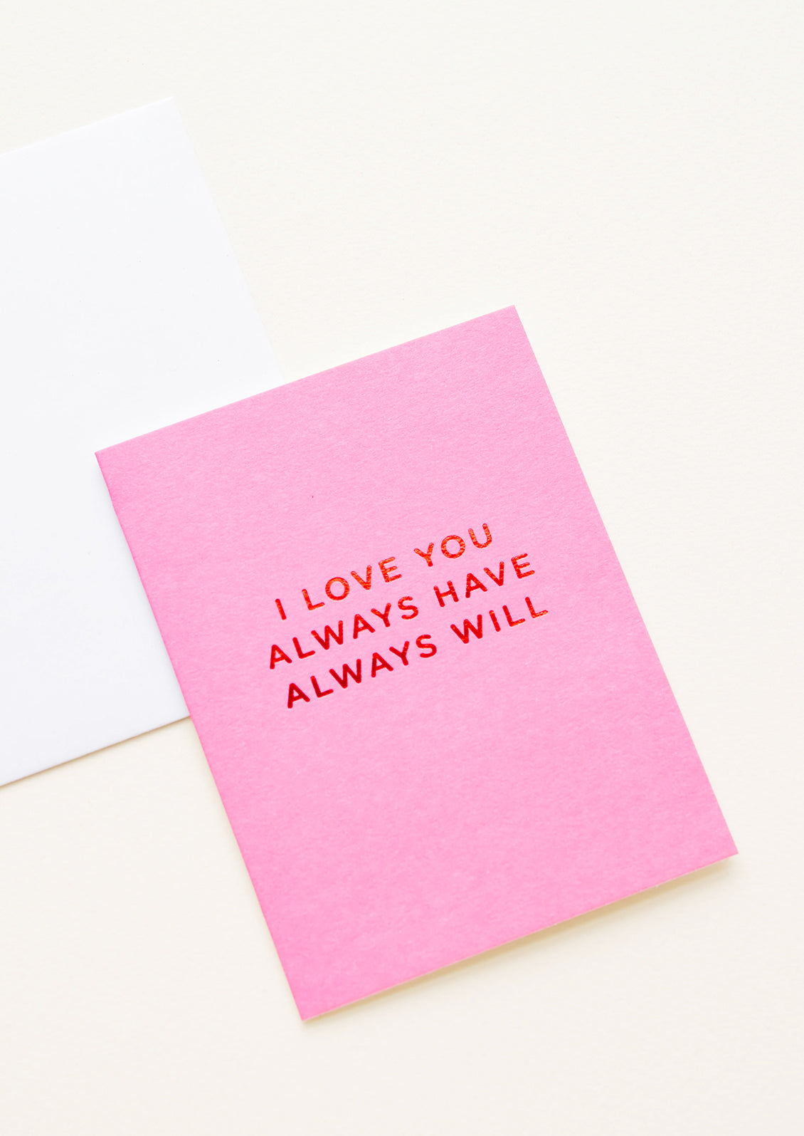 A white envelope and bright pink greeting card with the words "I love you always have always will" in red foil.