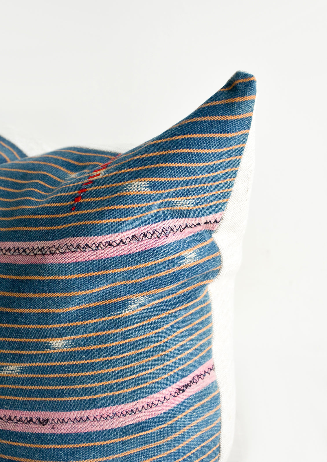 Indigo baule fabric pillow with thin orange and thicker pink stripes and small embroidered details