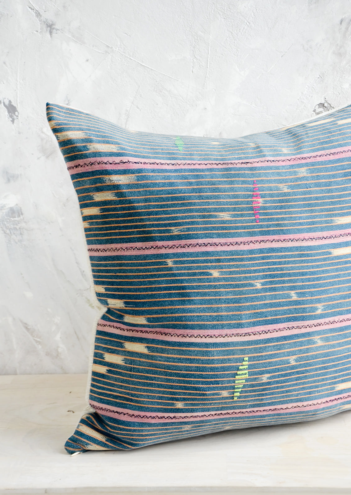 Throw pillow made from vintage indigo Baule fabric with peach and pink stripes and neon embroidery details