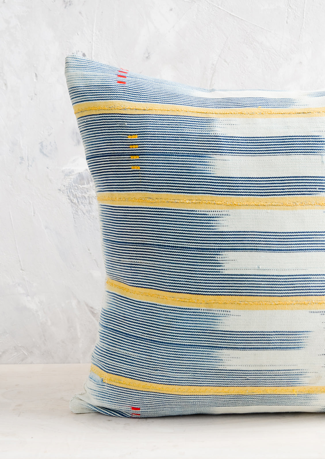A square throw pillow in vintage African baule indigo ikat fabric with yellow accents.