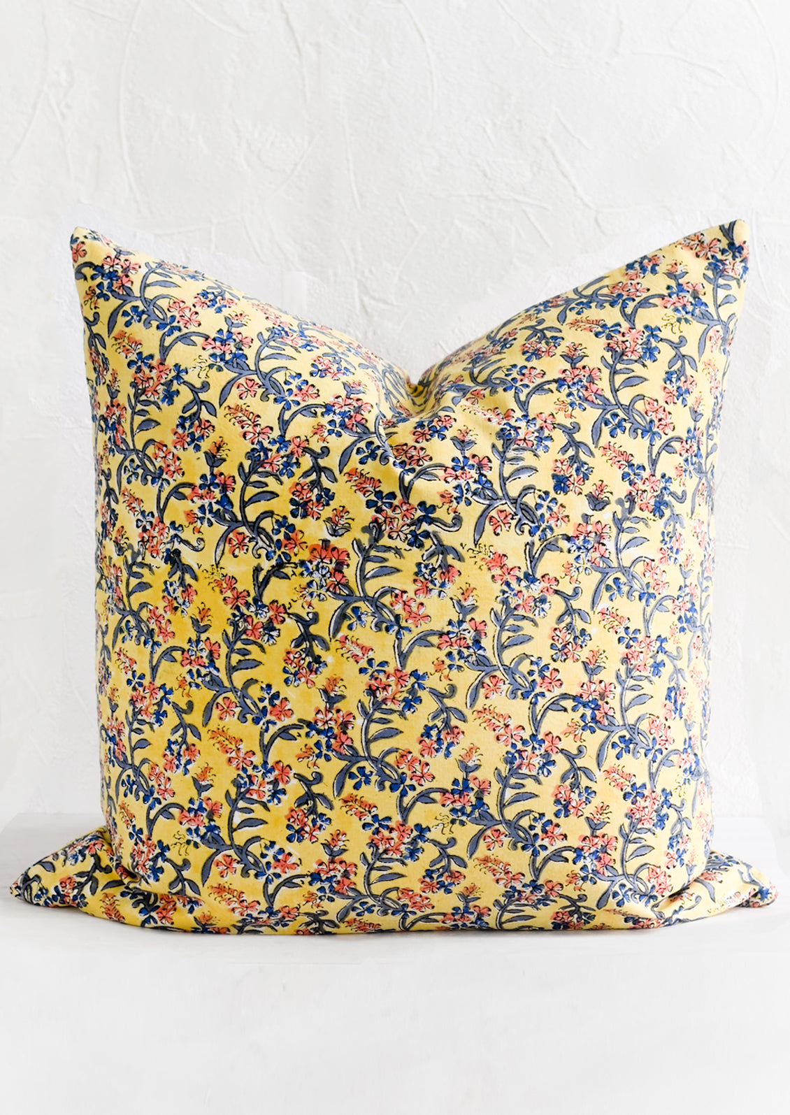 A block printed throw pillow in yellow with blue and pink floral print.