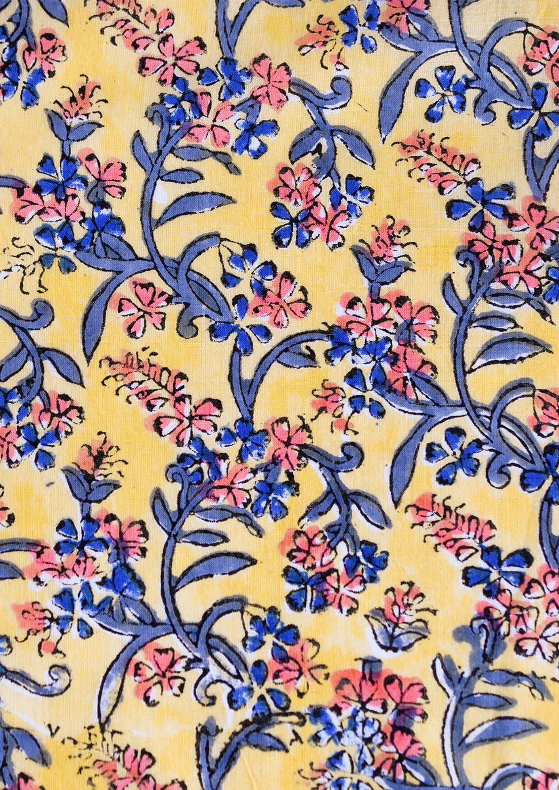 A block printed throw pillow in yellow with blue and pink floral print.