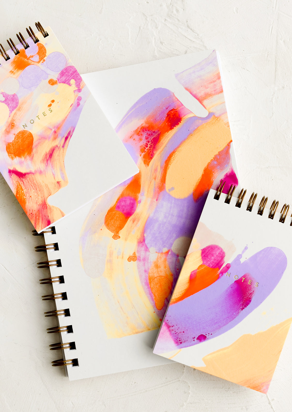 Vibrantly painted white notebooks with purple, pink and orange paint.