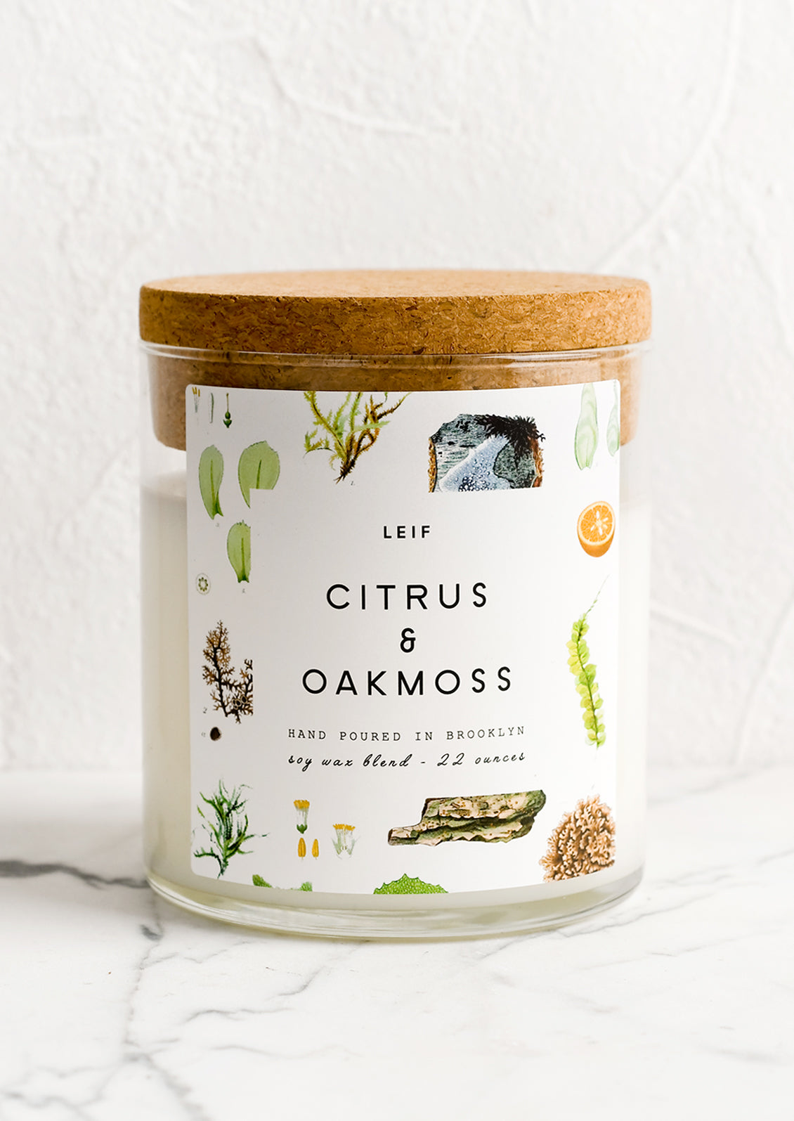 A glass candle with a cork lid and white botanical printed label reading "citrus and oakmoss".
