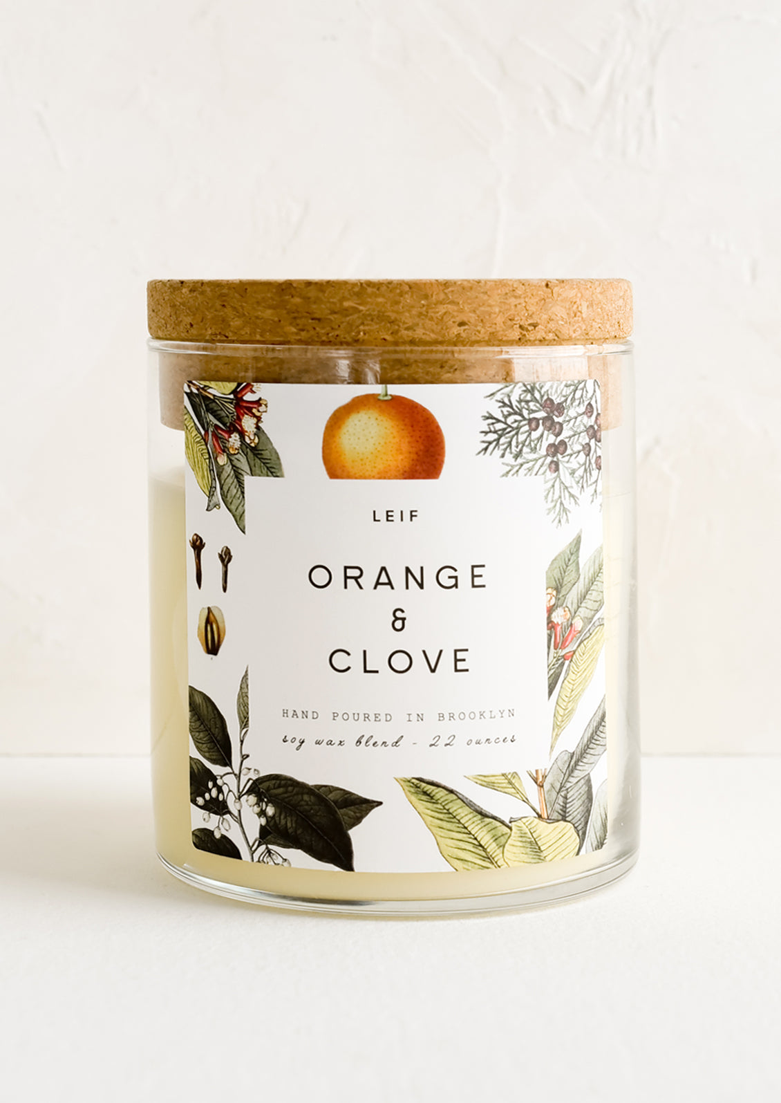 A glass jar candle in Orange & Clove scent with botanical print label.