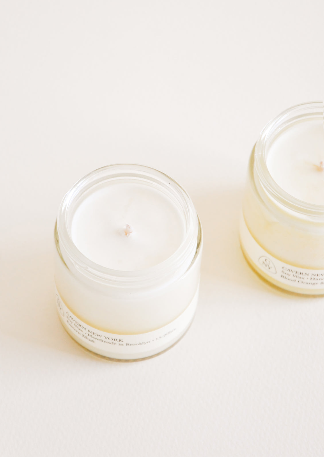 Two glass jars with white candle and wick inside