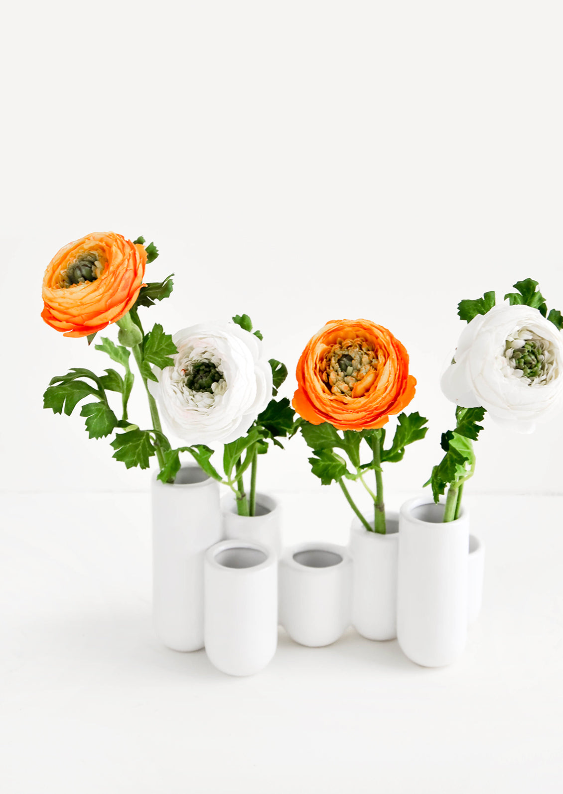 Multiple stem vase made of white ceramic vials in varying heights, clustered and fused together. Displayed with ranunculus flowers.