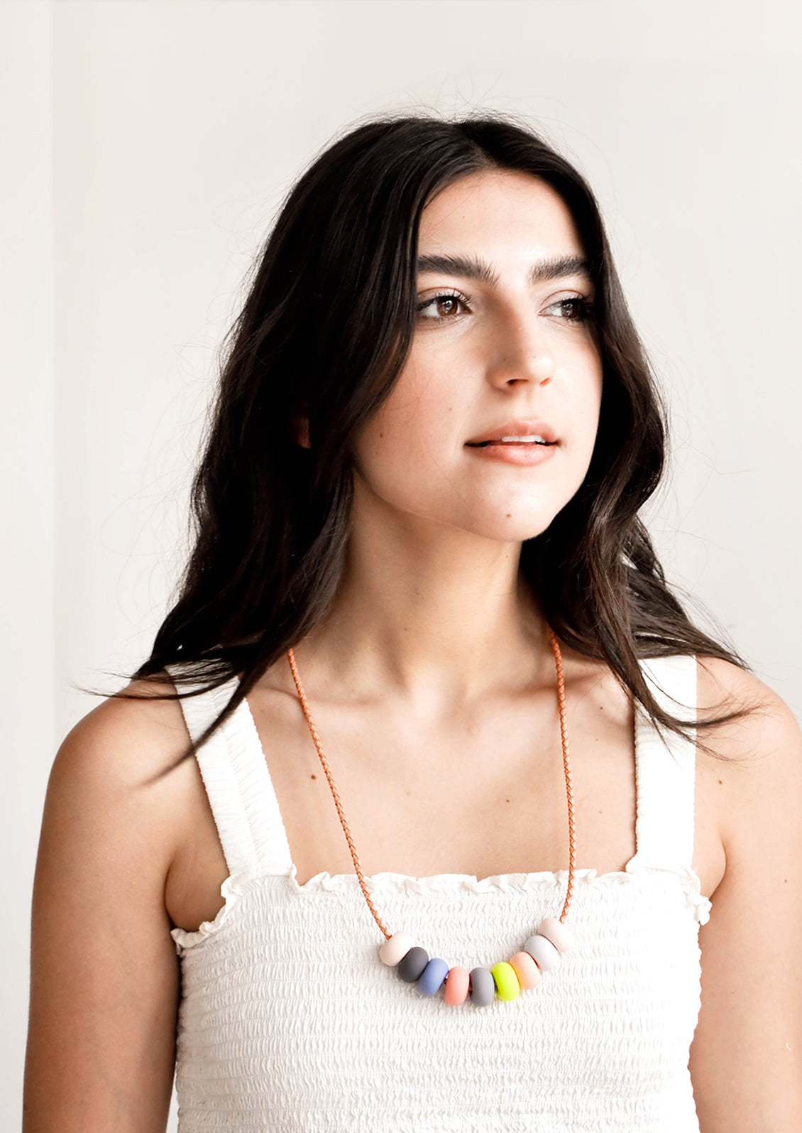 Model wears clay bead necklace and white tank top.