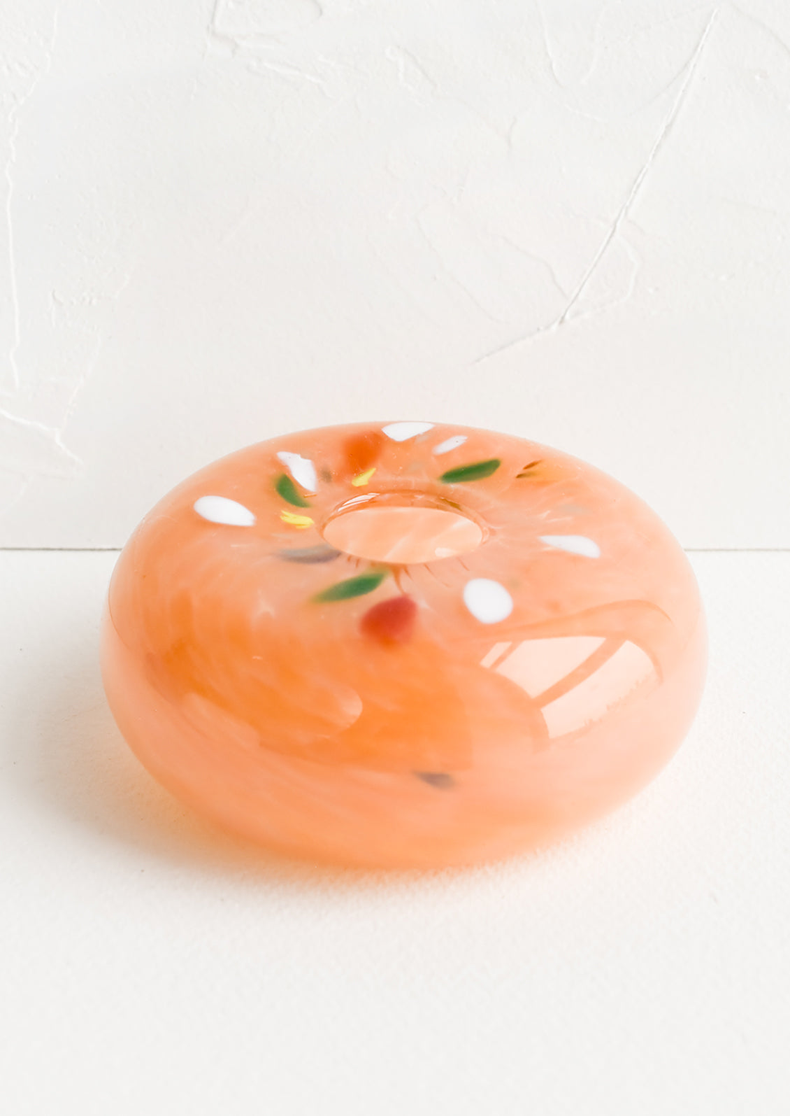 A glass bud vase in peach with colorful fleck detail around opening.