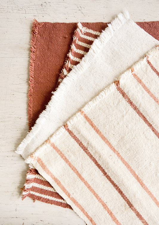 Four natural cotton placemats with frayed edges in a palette of cream, blush and terracotta