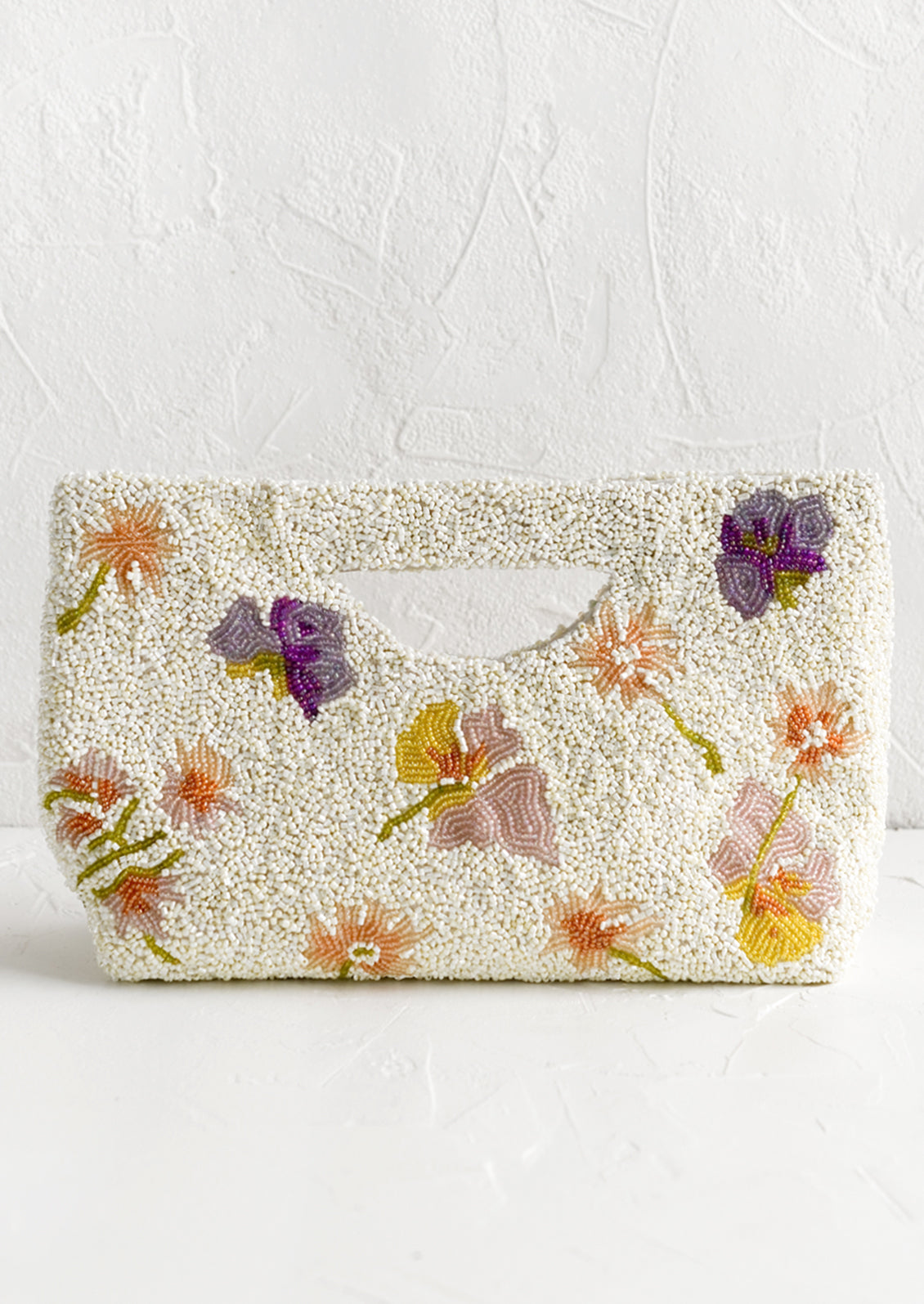 A white beaded east-west clutch with cutout handle and pastel floral pattern.