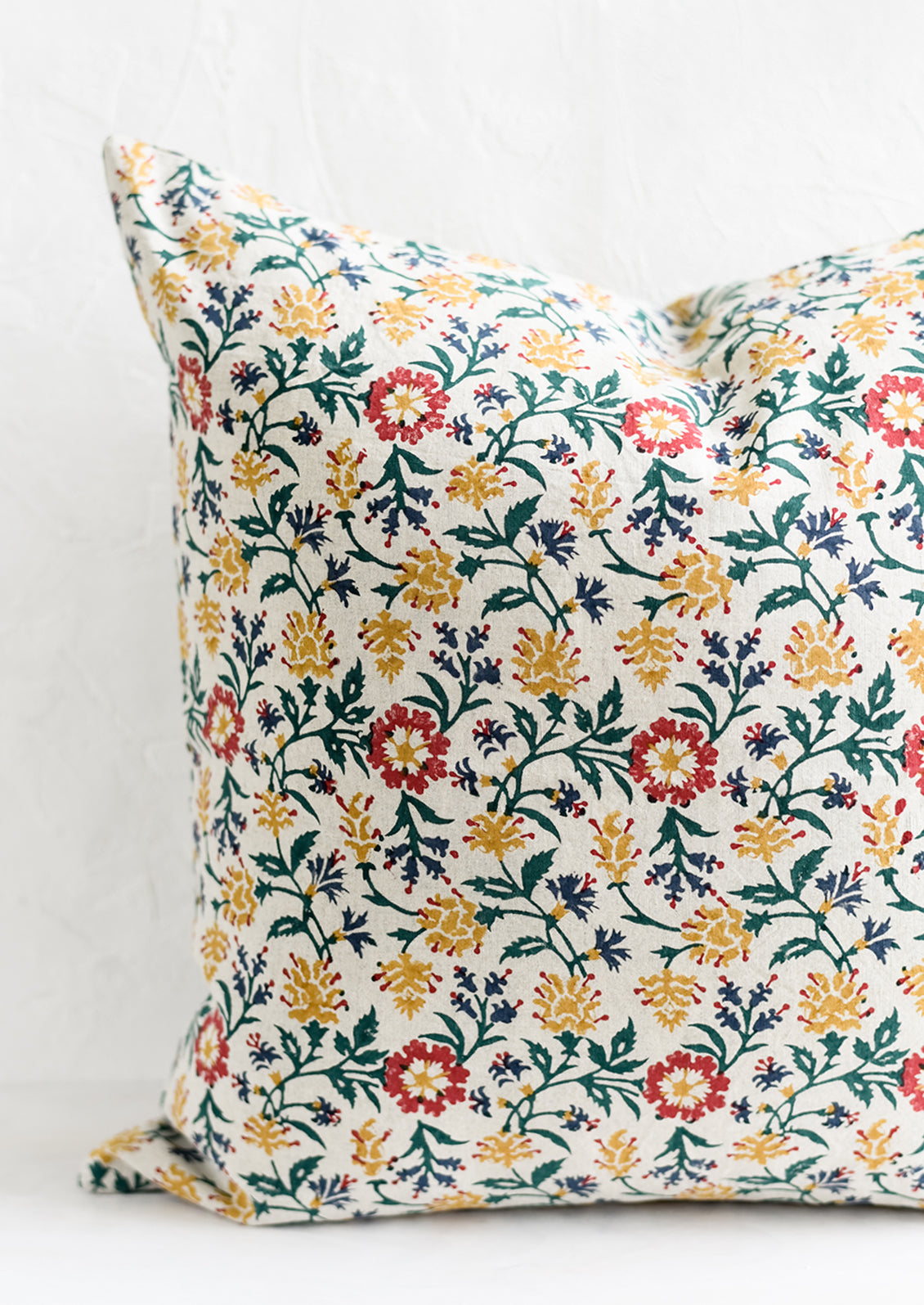 A block printed pillow in green, red, blue and yellow floral print.