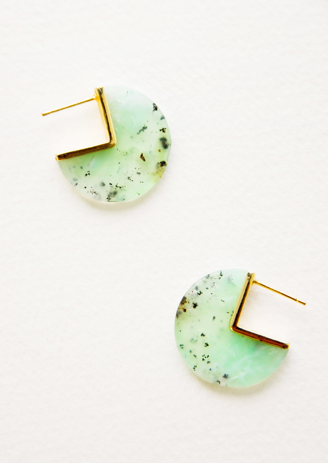 Three quarter disc shaped earrings of a semi-translucent blue-green gemstone speckled with brown flecks with gold hardware and post back.