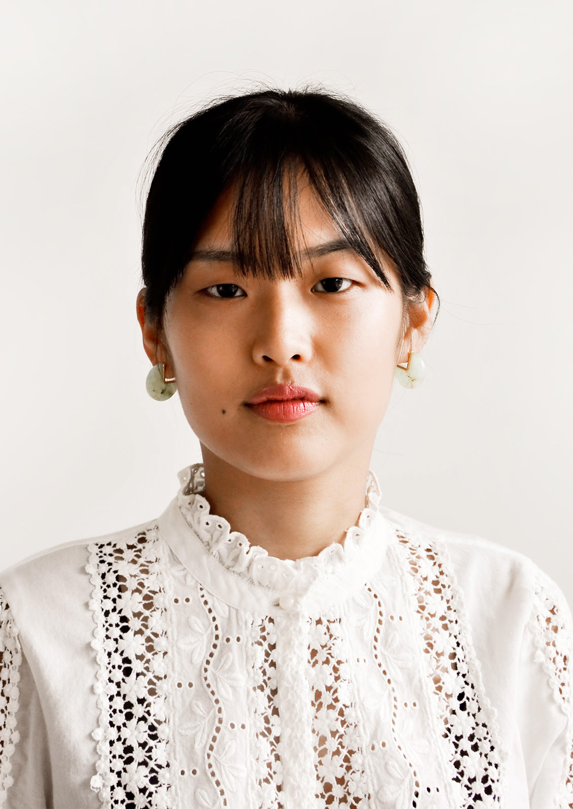 Model wears green gemstone earrings and white blouse.