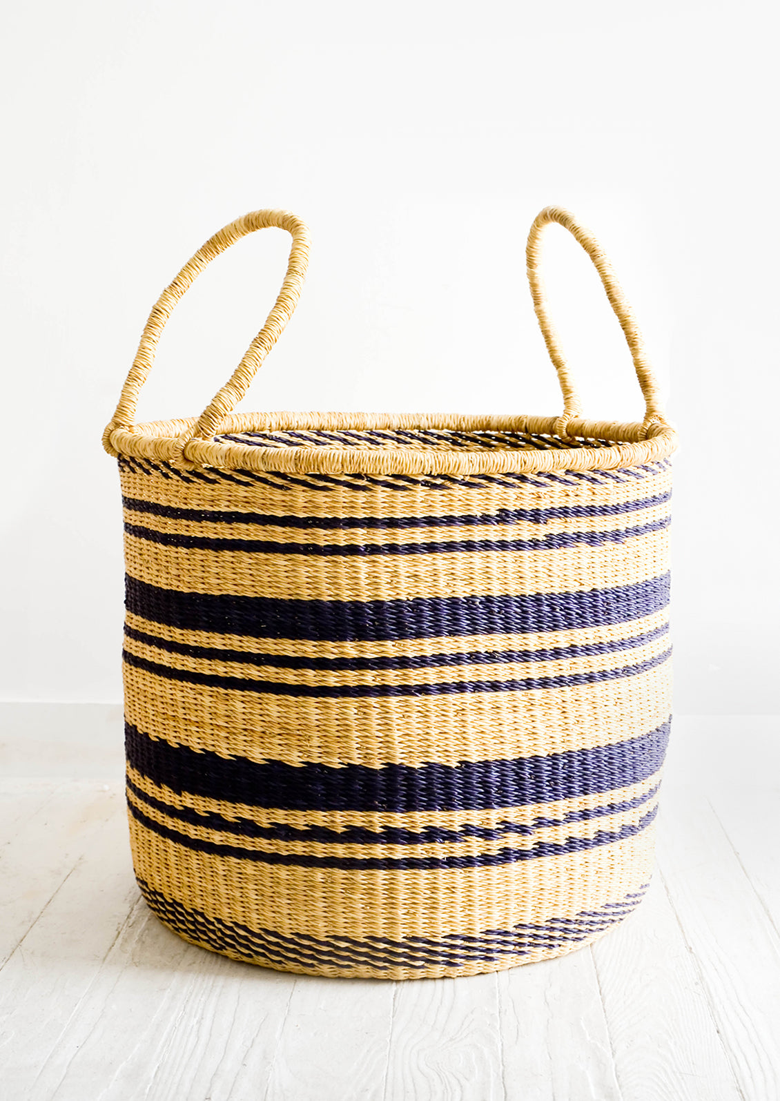 Round straw storage basket with handles at top and navy blue stripes throughout