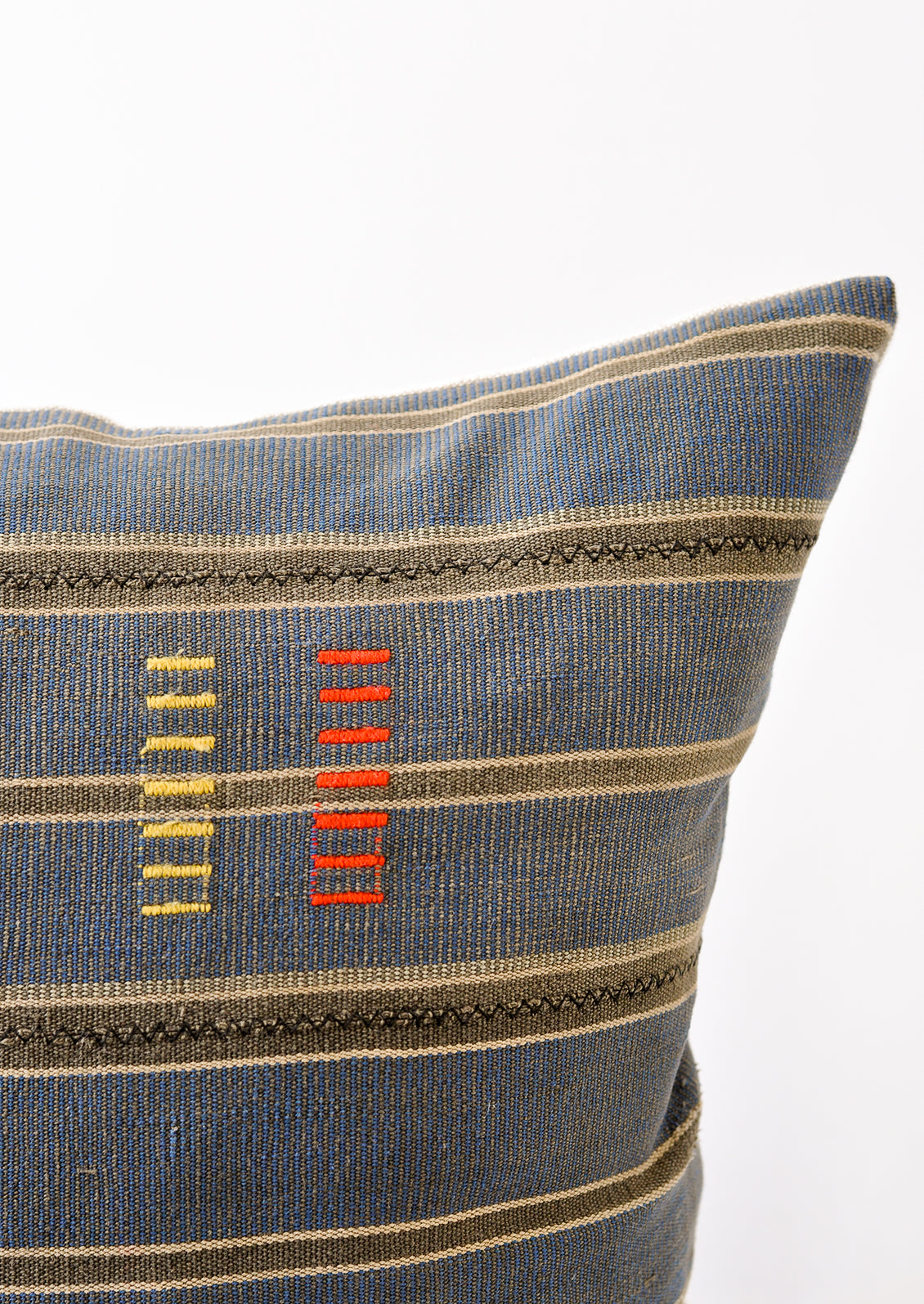 A detailed shot of an indigo and dark grey striped pillow, focusing on the yellow and red dash embroidery.