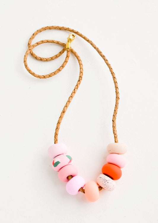 Necklace made from round clay beads in pink hues strung on braided leather cord