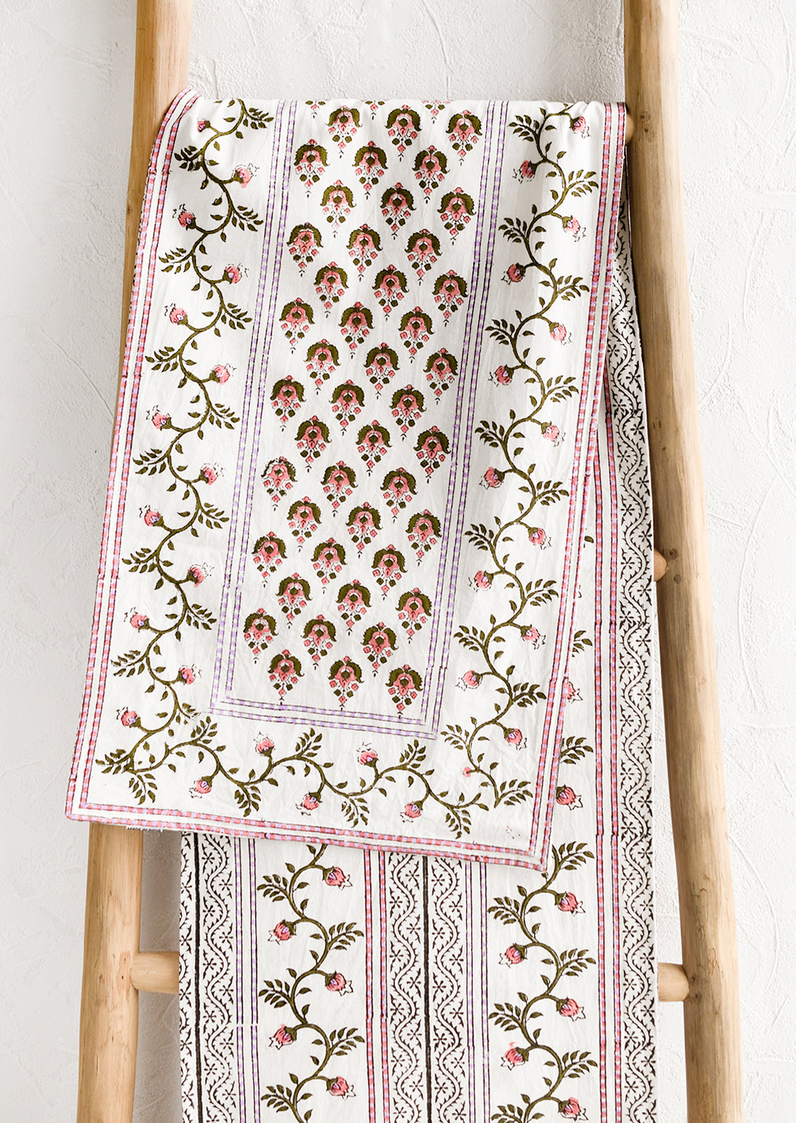 A block printed white table runner with pink, green and lavender floral print.