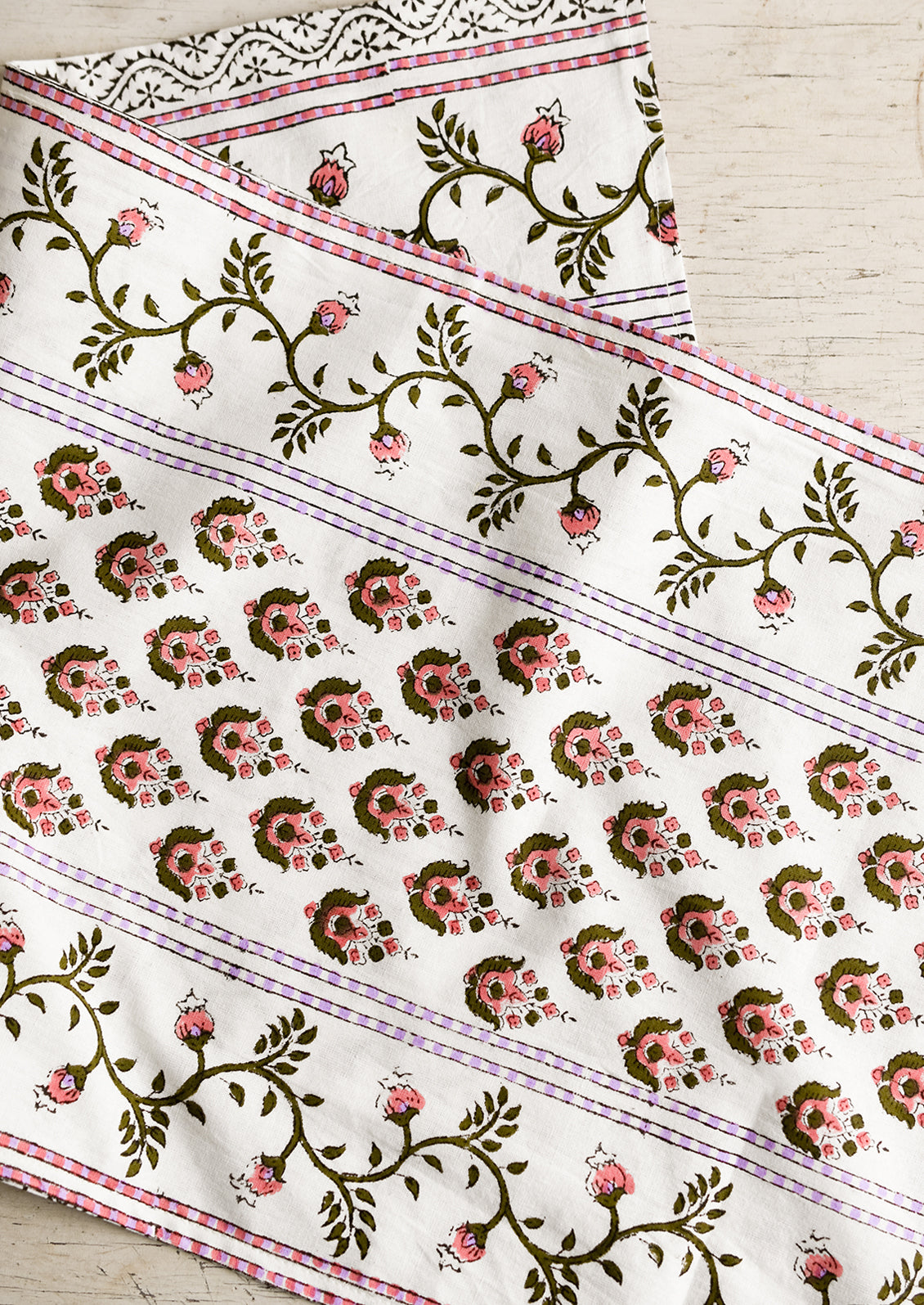 A block printed white table runner with pink, green and lavender floral print.