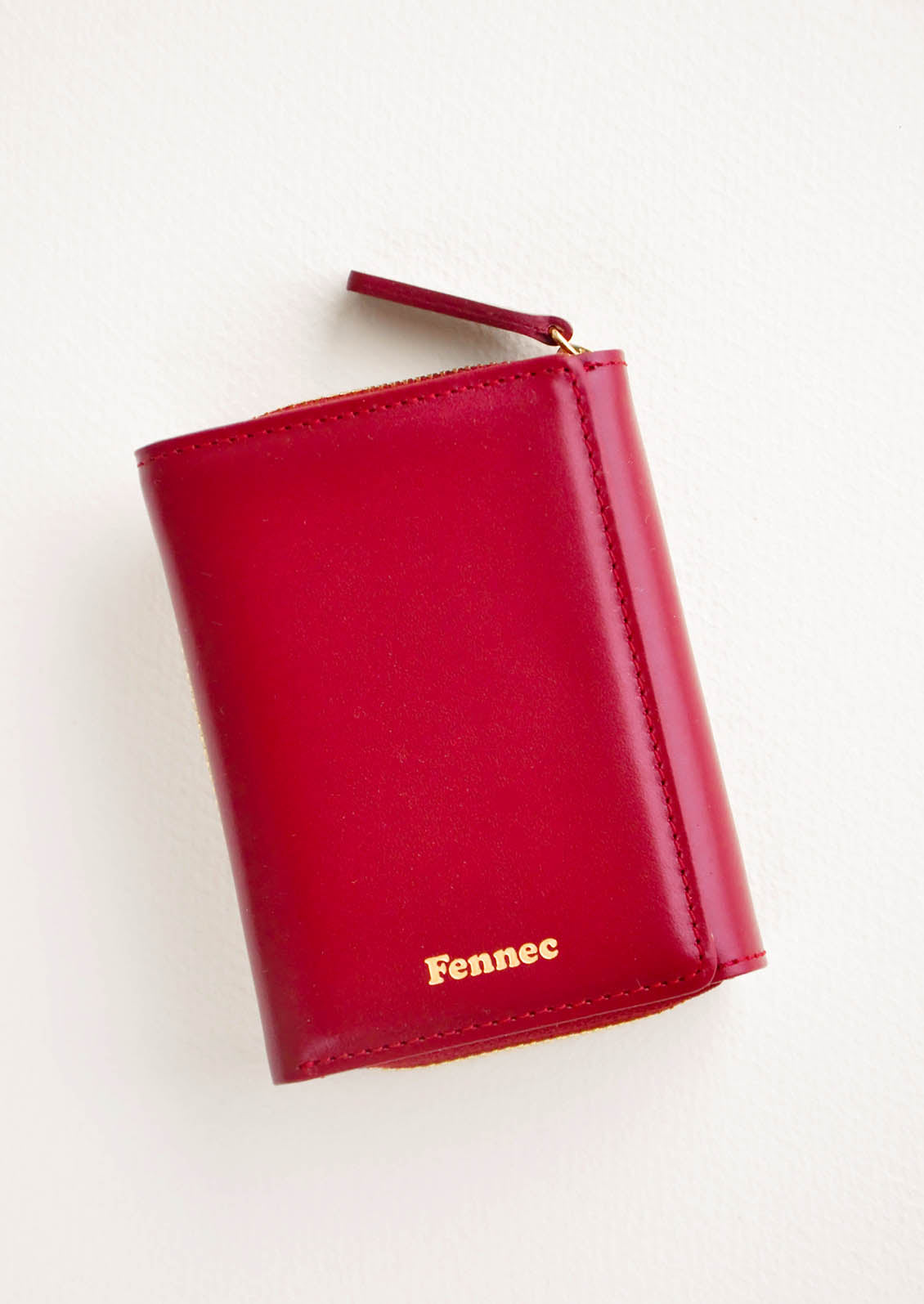 Dark red leather wallet that zips on three sides, in a closed position, with matching tab pull.