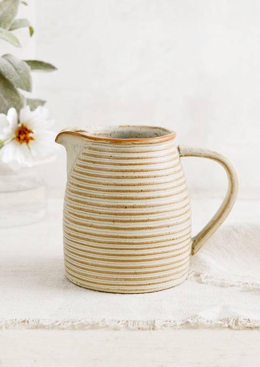 A tan ceramic pitcher with striped texture.