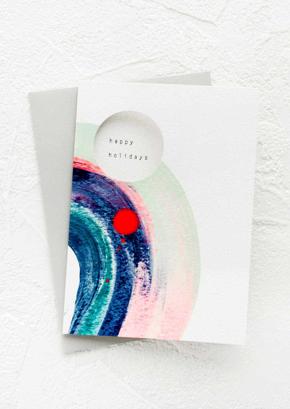 A small greeting card with circular cutout on front revealing text reading "Happy holidays".