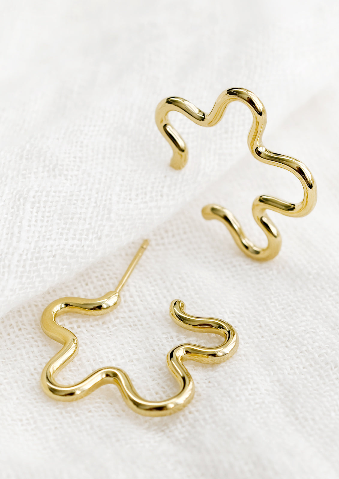 A pair of gold flower outline earrings.