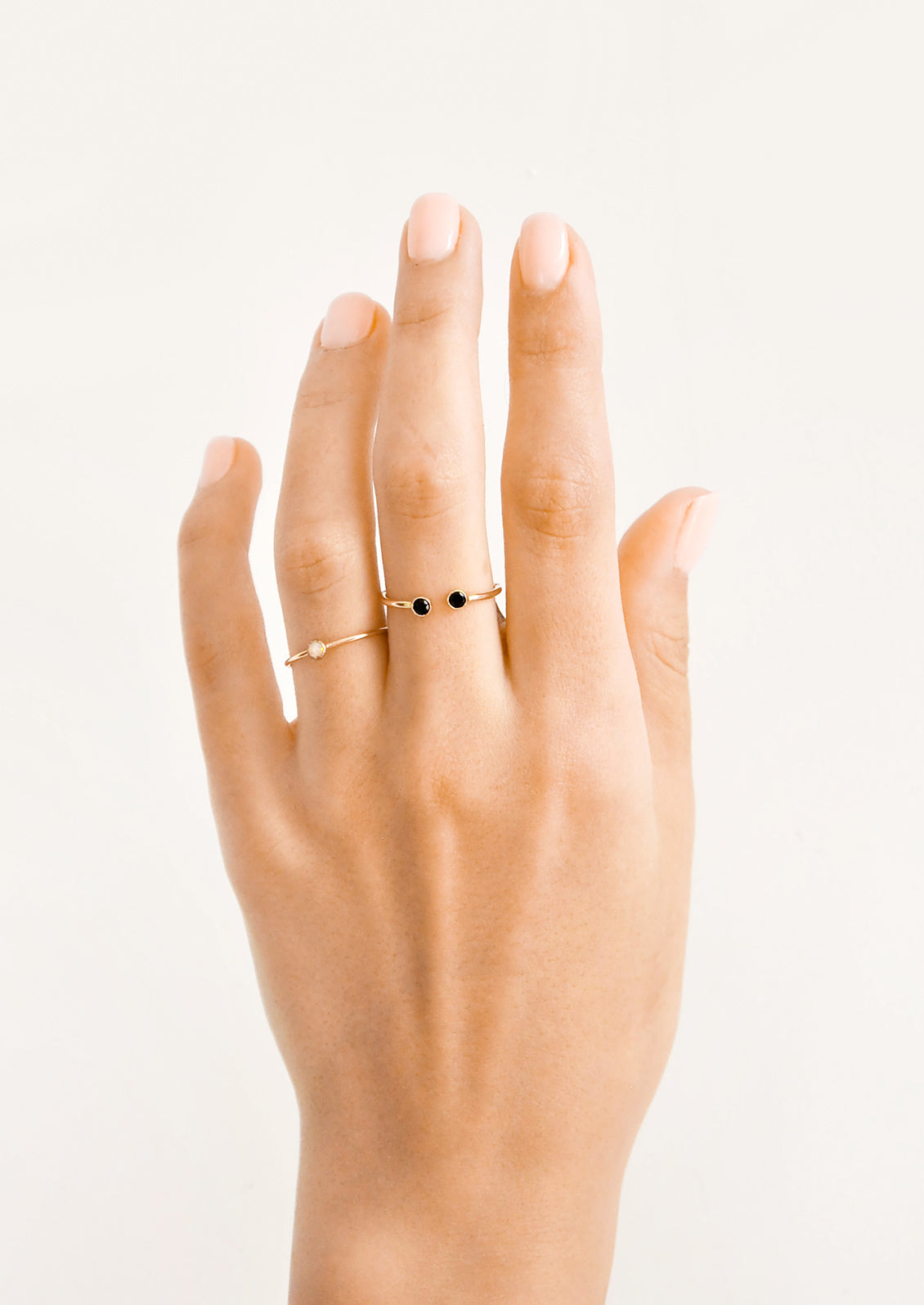 Model shot of hand wearing two gold rings with stones.