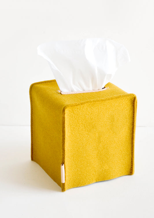 Cube-shaped tissue box cover made from felted wool in mustard color with leather accents