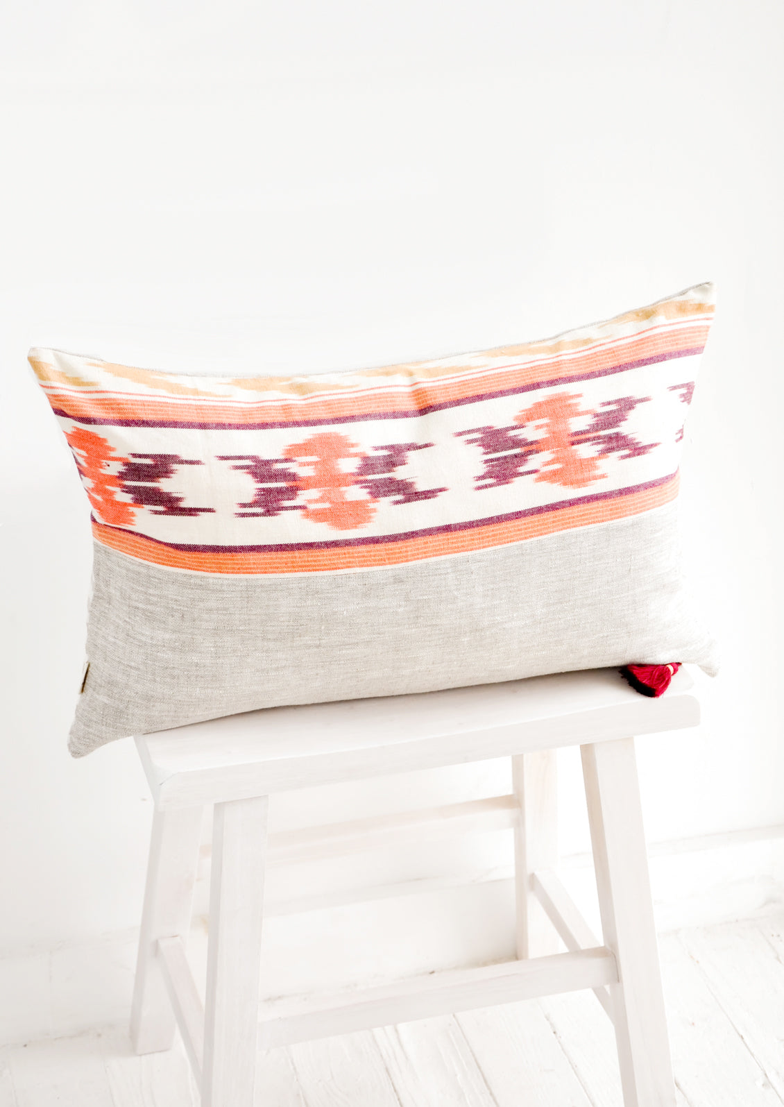 Rectangular throw pillow in mixed fabrics. Top half is ikat print in orange and red, bottom half is plain linen.