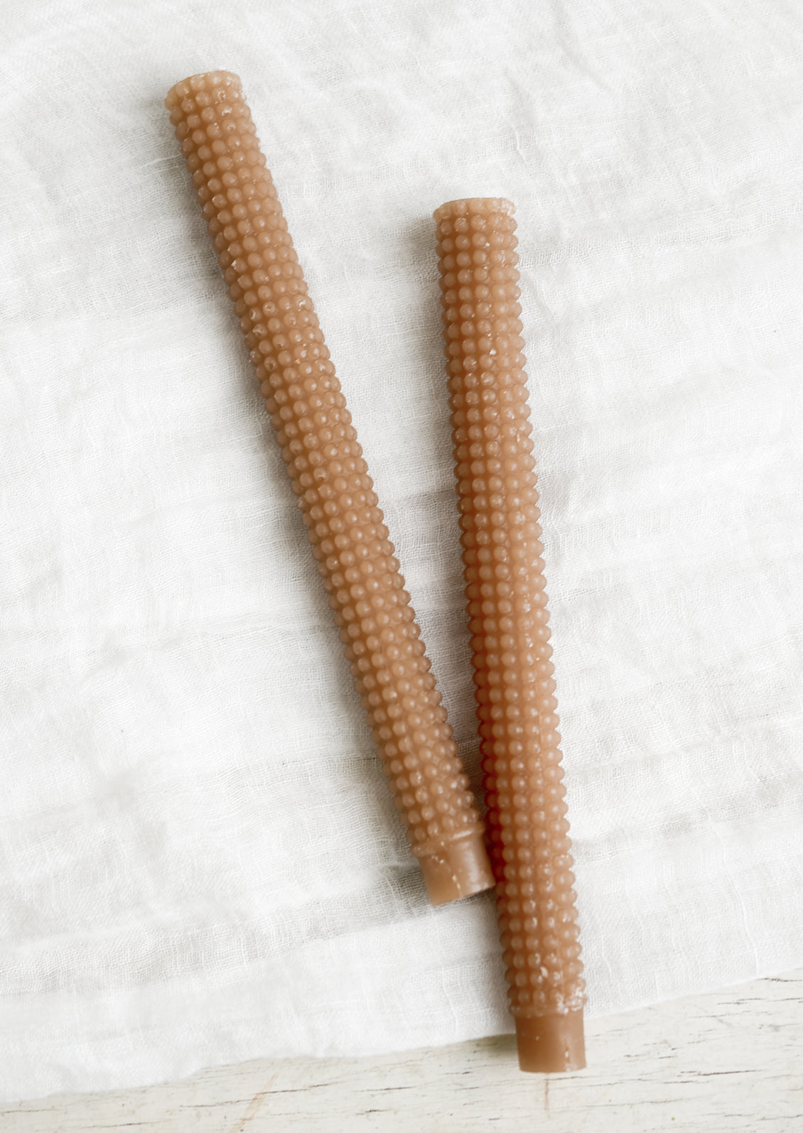 A pair of hobnail textured taper candles in fawn brown.