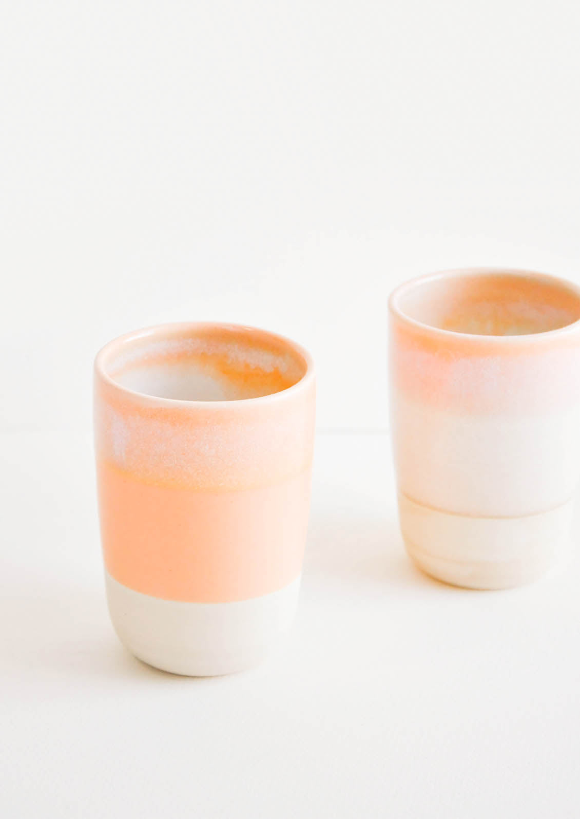 Two ceramic tumblers with unfinished bottoms and orange glaze.