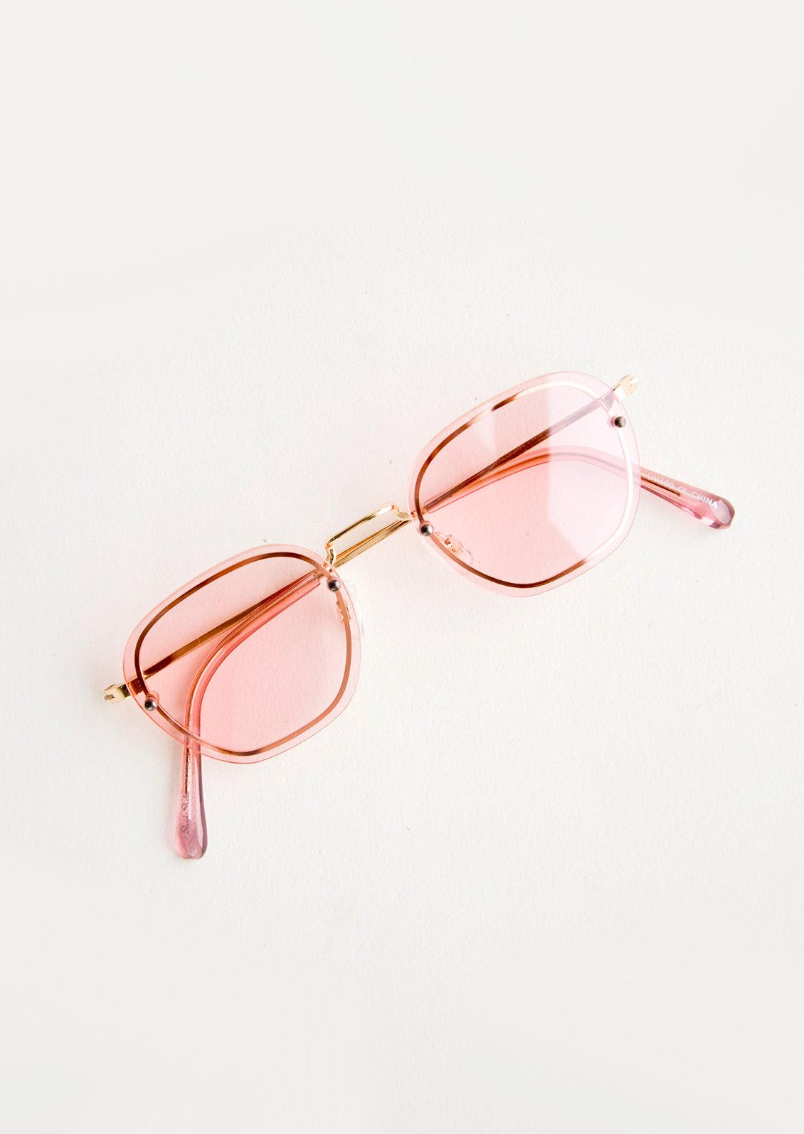 Sunglasses with light pink tinted plastic lenses and a metal frame behind the lens