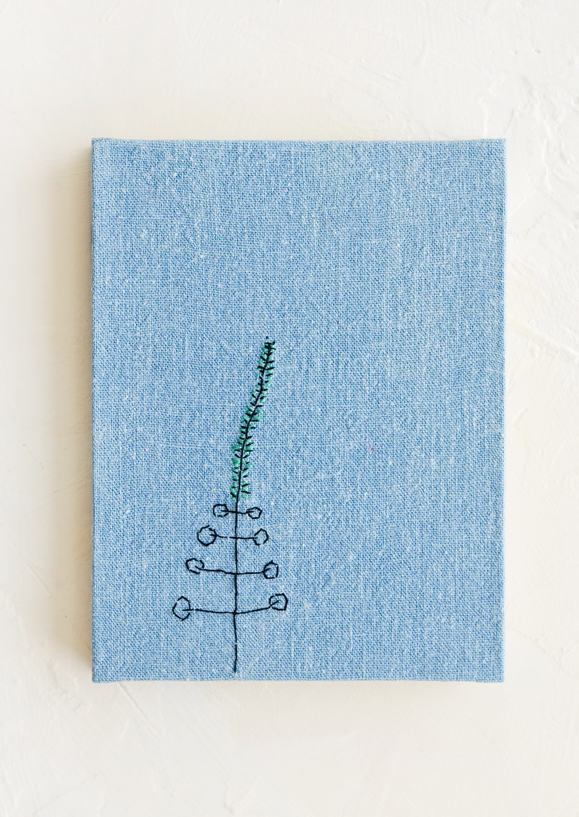A blue cloth covered journal with botanical embroidery detail.